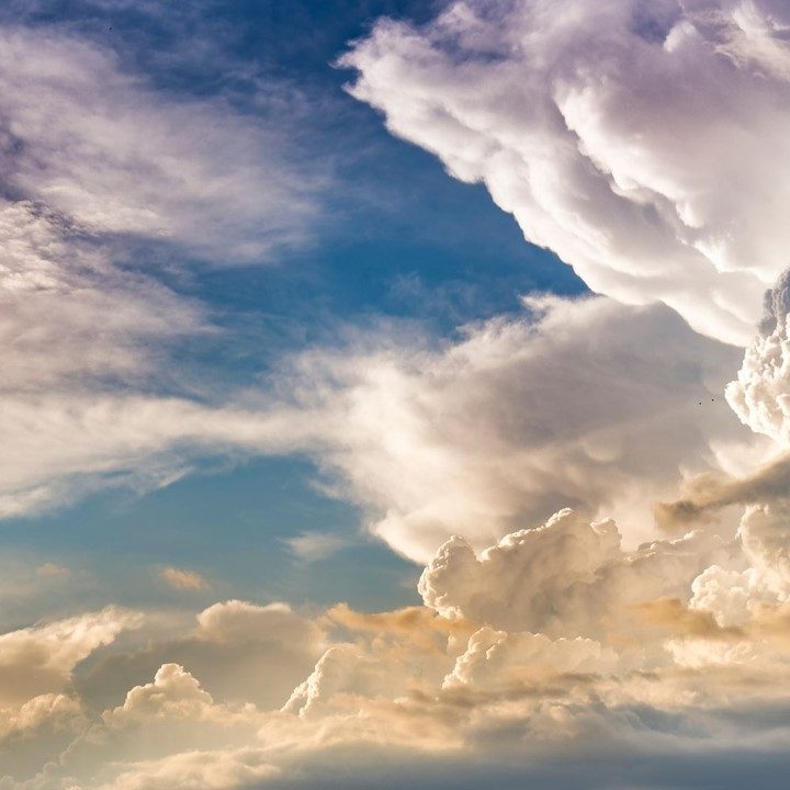 Fluffy white clouds in a blue sky with hints of orange and pink at sunset.